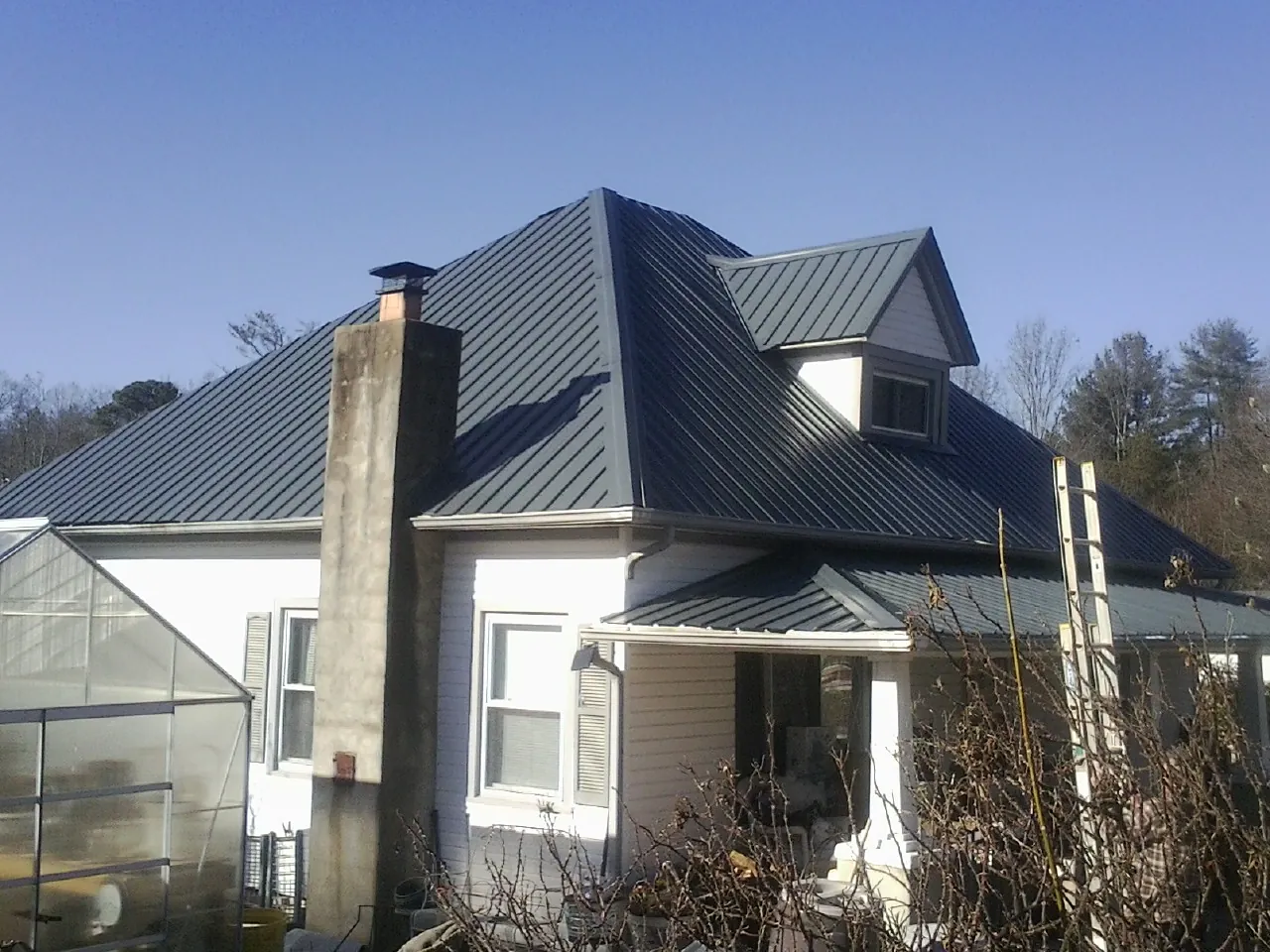 Dark blue standing seam metal roof on a white farmhouse with dormer — Slate & Tile Roof Repair by Roofing Brothers in Hardin