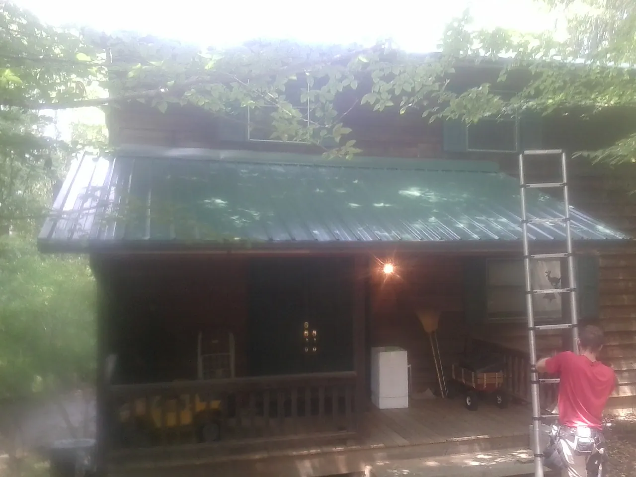 Worker on a ladder at the green porch roof of a wooded cabin in Hardin